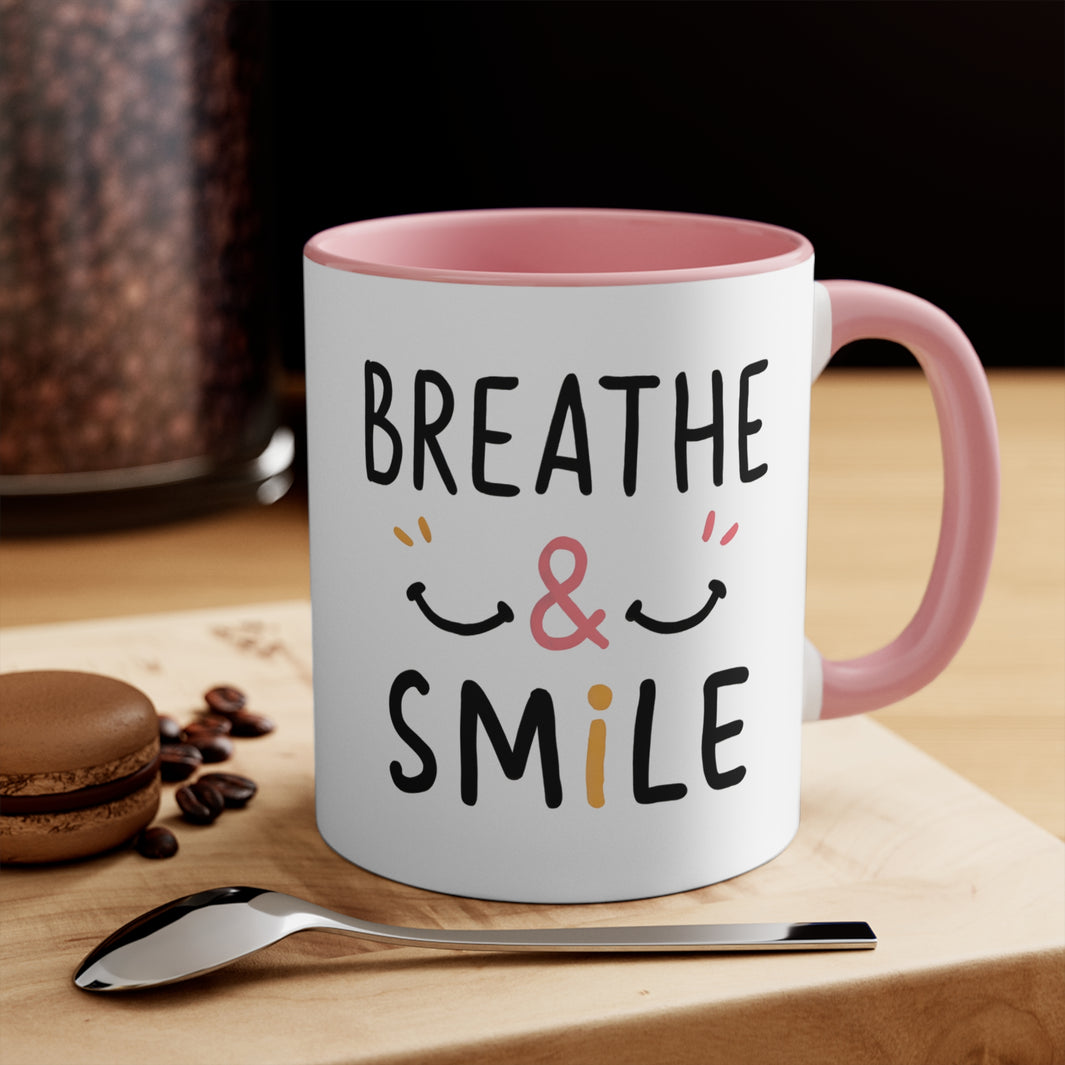 A white and pink rim coffee mug with caption of Breathe & Smile happy smile there are two adjoining smiley faces