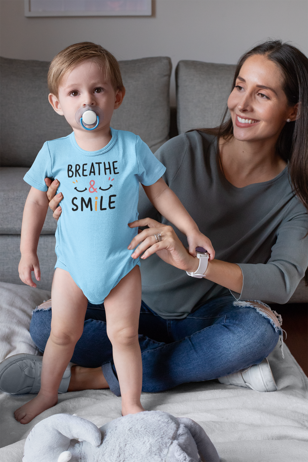 Mom holding her happy baby boy wearing a onesie with the words breathe & Smile