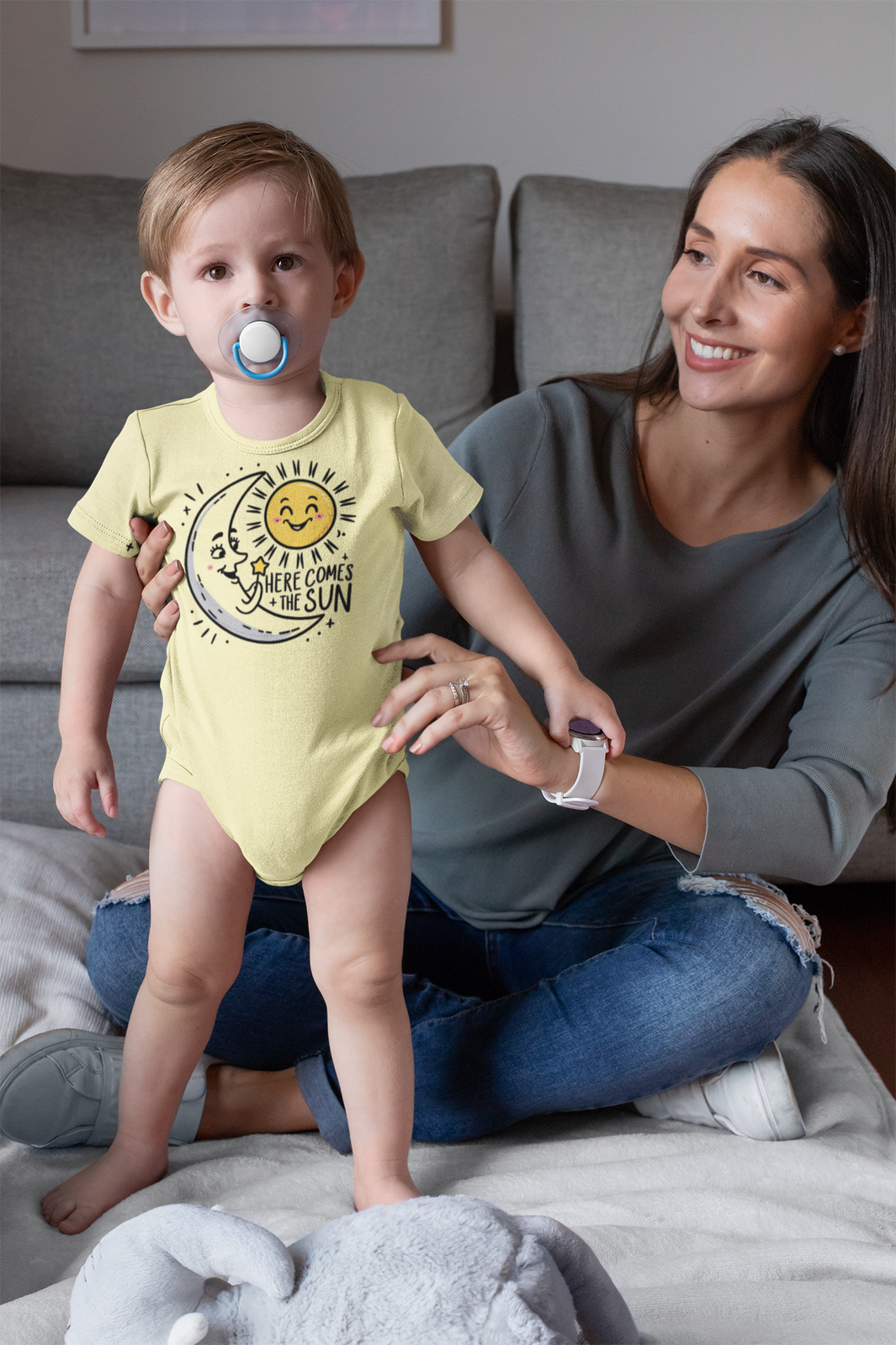 A mom and son on the couch a onesie with the moon greeting the sun with the caption here comes the sun