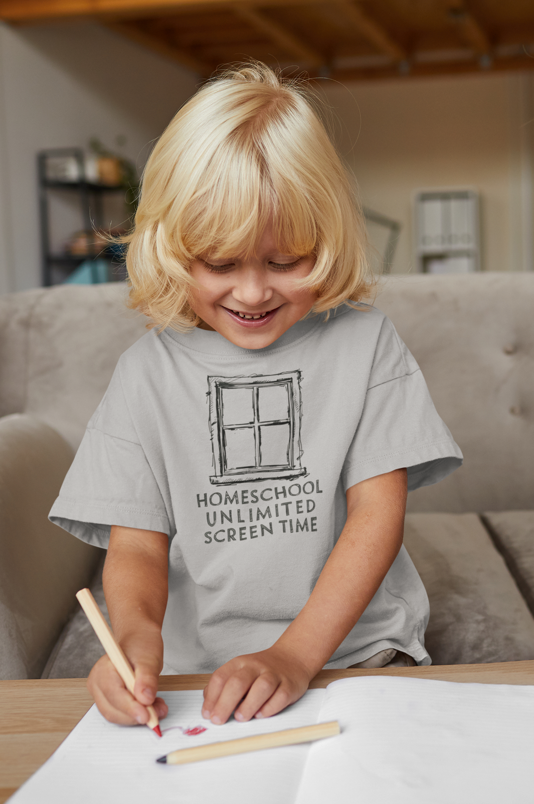 a blonde haired boy writing on table wearing a t-shirt with homeschool unlimited screen time